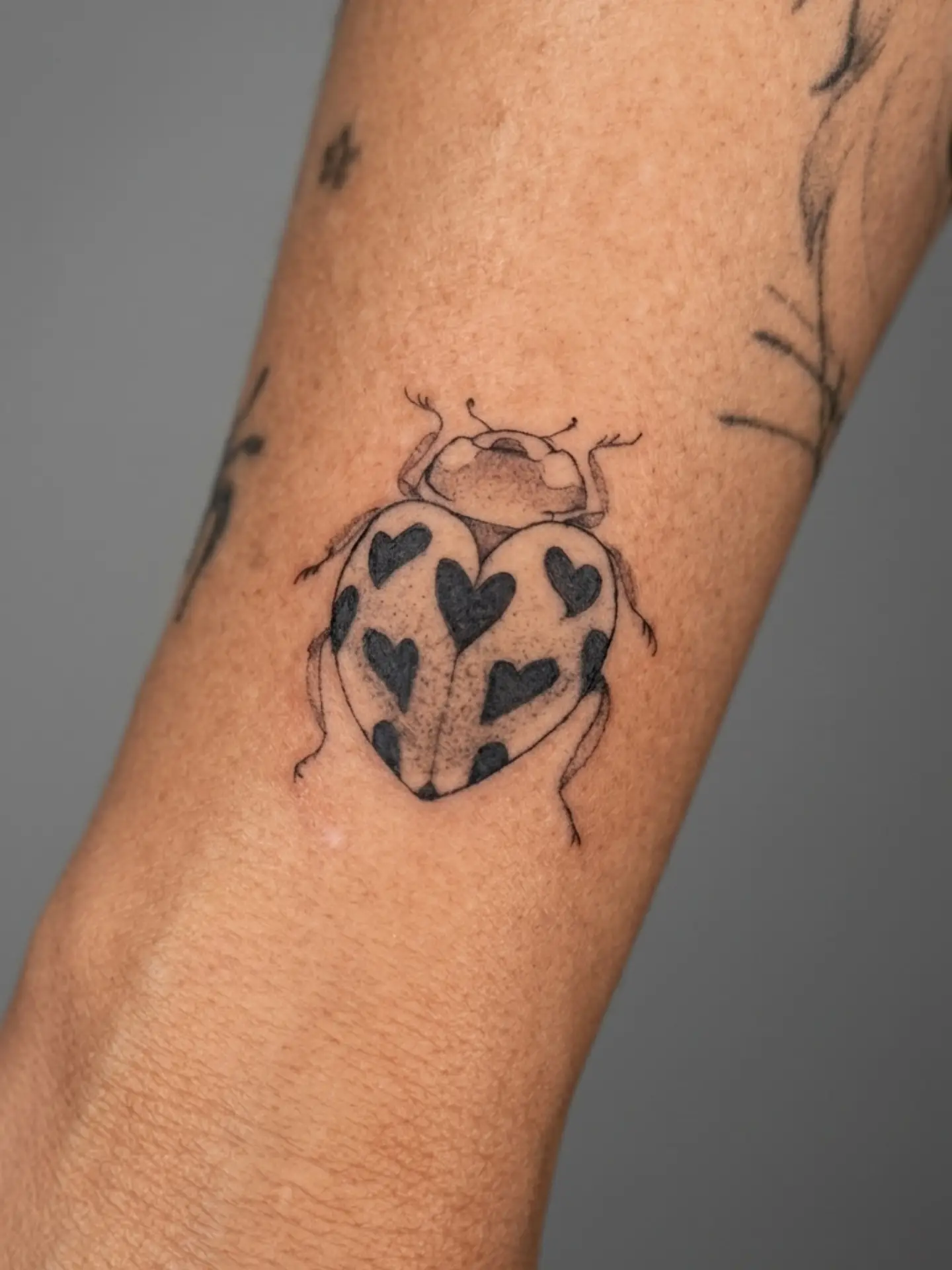 Fineline tattoo van een lieveheersbeestje met hartjes